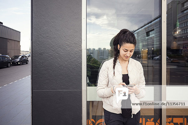 Young woman using smart phone against window