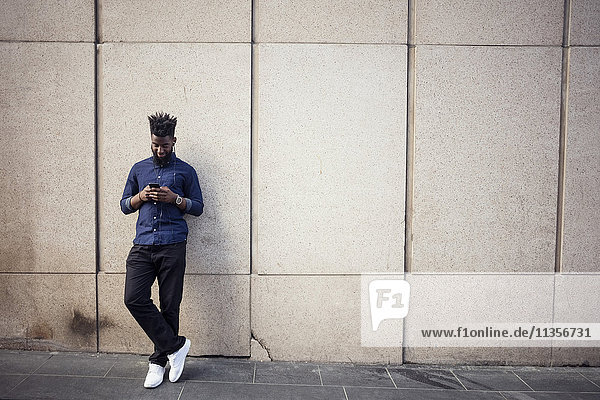 Man listening to music from mobile phone against wall