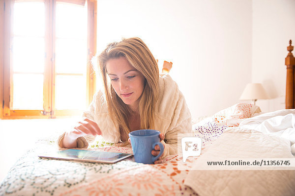 Junge Frau liegt im Bett und stöbert morgens auf einem digitalen Tablet