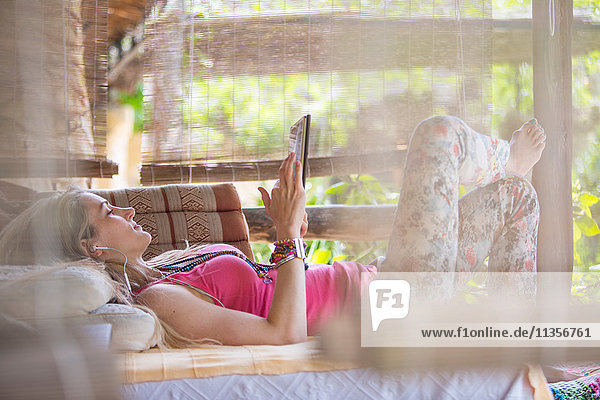 Junge Frau entspannt sich auf der Veranda und stöbert auf digitalem Tablet