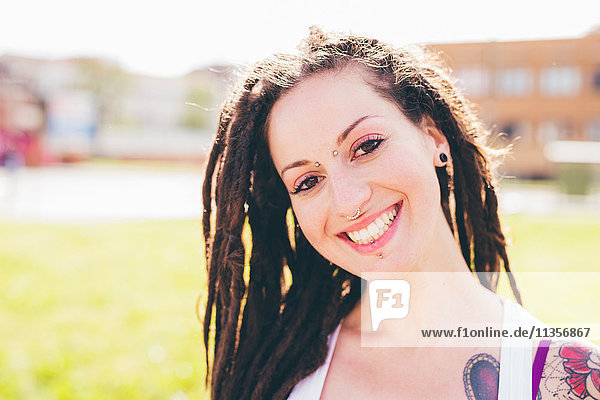 Portrait of tattooed young woman with dreadlocks in urban park