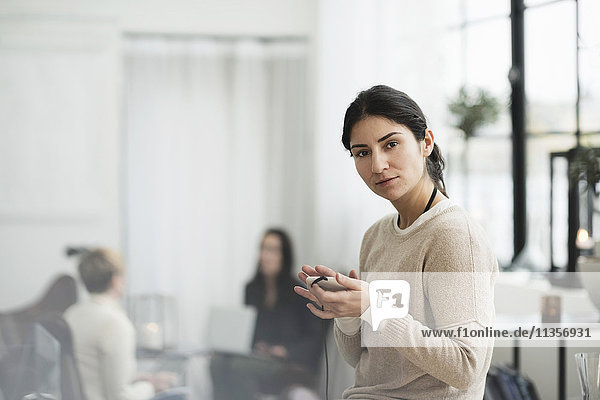 Porträt einer Geschäftsfrau mit Handy und Kollegen im Hintergrund