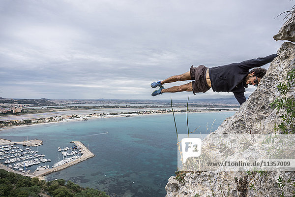 Männlicher Bergsteiger balanciert horizontal mitten in der Luft auf einem Küstenfelsen  Cagliari  Italien