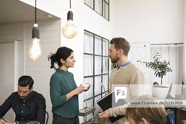 Businesswoman talking with man while colleagues working at office