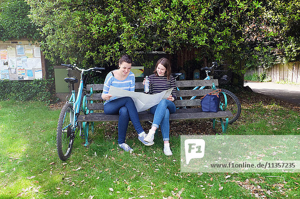 Junge erwachsene Schwestern mit Fahrrädern sitzen auf einer Bank und schauen auf die Karte
