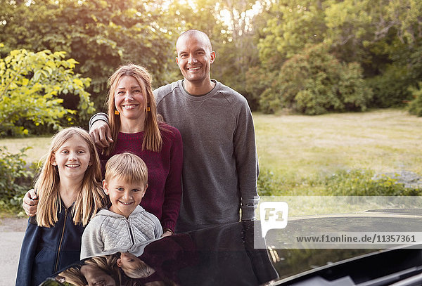 Portrait of happy family standing by black electric car at park