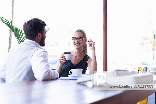 Erwachsener Mann und Frau  die vor einem Café sitzen  Kaffee trinken  von Angesicht zu Angesicht  lächelnd