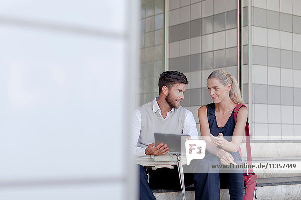 Reifer Mann und Frau sitzen im Freien und schauen auf ein digitales Tablet