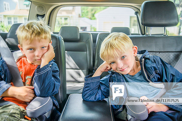 Twin brothers sitting in back of vehicle  bored expressions