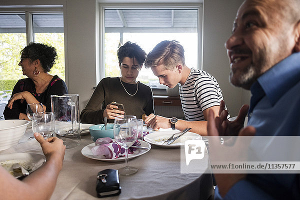 Friends using phone while family talking at dining table in dinner party