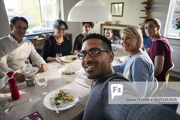 Porträt eines lächelnden Mannes  der sich mit seiner Familie und seinen Freunden auf einer Dinnerparty vergnügt.
