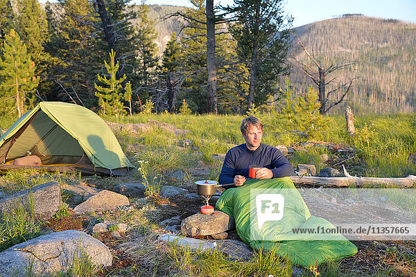 Männlicher Camper im Schlafsack bereitet am Midnight Ridge  Colville National Forest  Bundesstaat Washington  USA  eine Mahlzeit auf dem Campingkocher zu