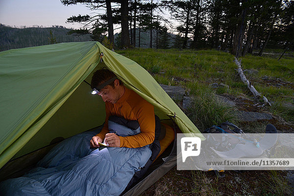 Männlicher Camper im Schlafsack beim Schreiben seines Tagebuchs in der Dämmerung am Midnight Ridge  Colville National Forest  Bundesstaat Washington  USA