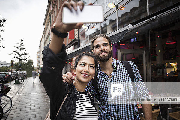 Paar  das Selfie durch Smartphone nimmt  während es am Straßencafé in der Stadt steht.