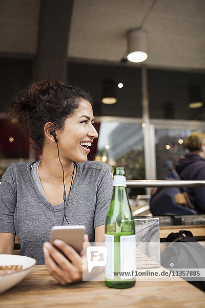 Happy woman wearing headphones resting at sidewalk cafe