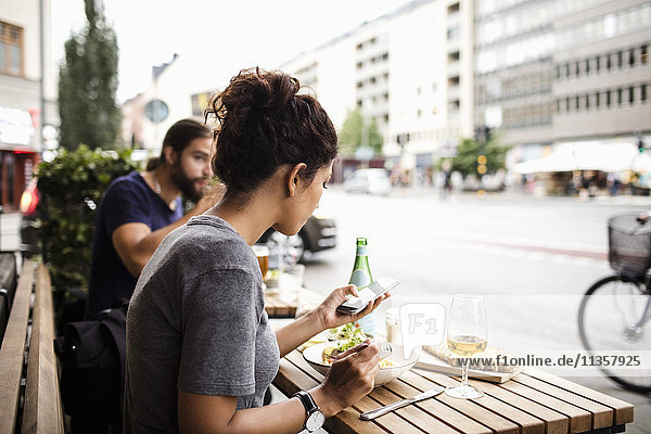 Frau beim Essen mit dem Handy im Straßencafé in der Stadt