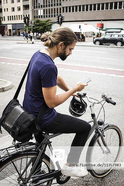Man with bicycle using mobile phone while standing on city street