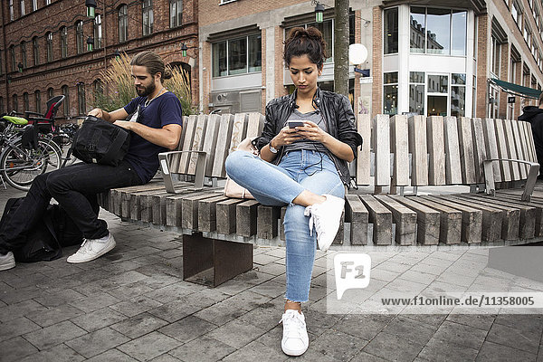 Low angle view of man and woman sitting on wooden bench against building in city
