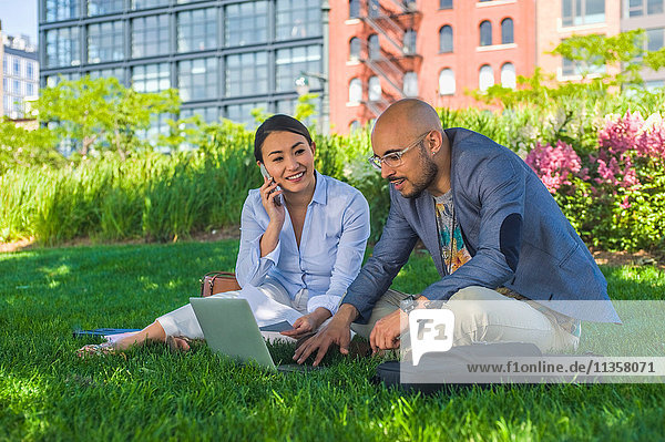 Geschäftsmann und -frau sitzen draußen auf dem Rasen und benutzen einen Laptop