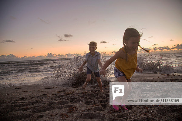 Junge und Schwester laufen bei Sonnenaufgang vor den plätschernden Wellen weg  Blowing Rocks Preserve  Jupiter Island  Florida  USA