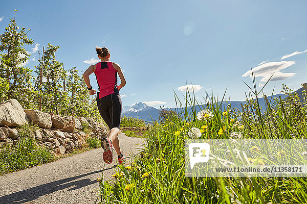 Young woman running along rural road  rear view  Meran  South Tyrol  Italy