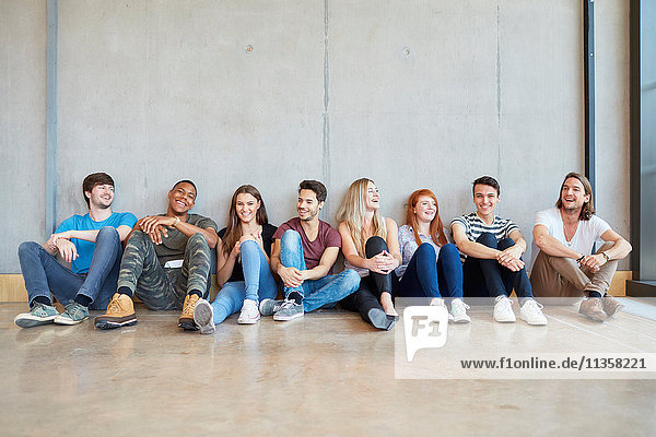 Gruppenbild von männlichen und weiblichen Studenten  die in einer Reihe auf dem Boden einer Hochschule sitzen