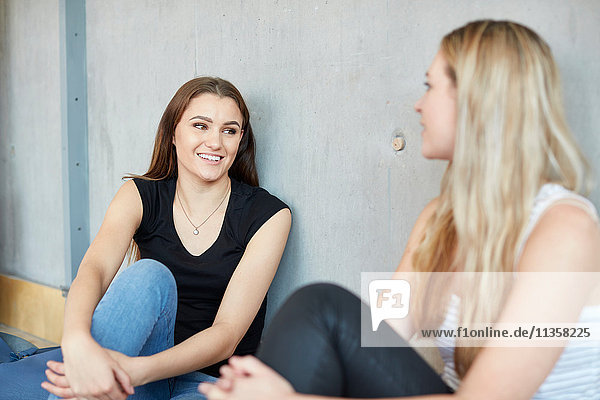 Two young female students sitting on floor chatting at higher education college