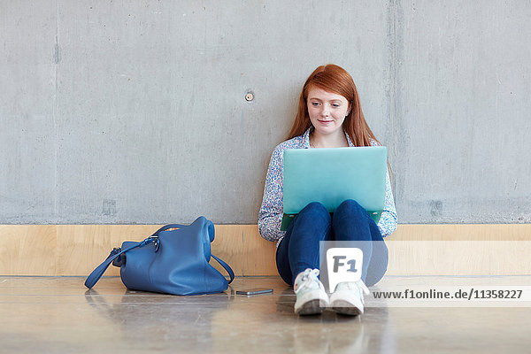 Junge Studentin mit Laptop am Boden sitzend an einer Hochschule