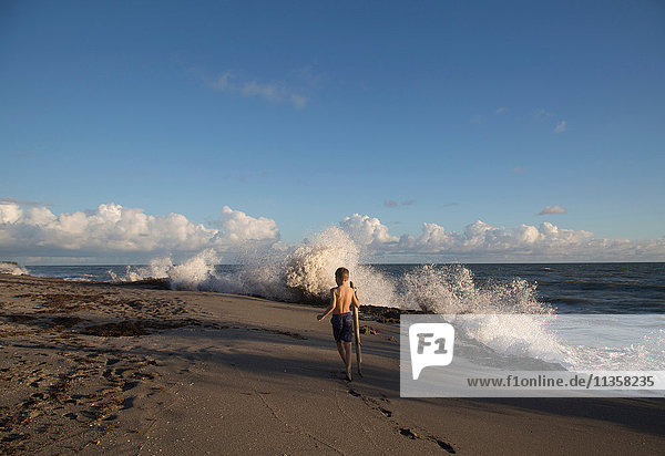 Rear view of boy exploring beach with splashing waves  Blowing Rocks Preserve  Jupiter Island  Florida  USA