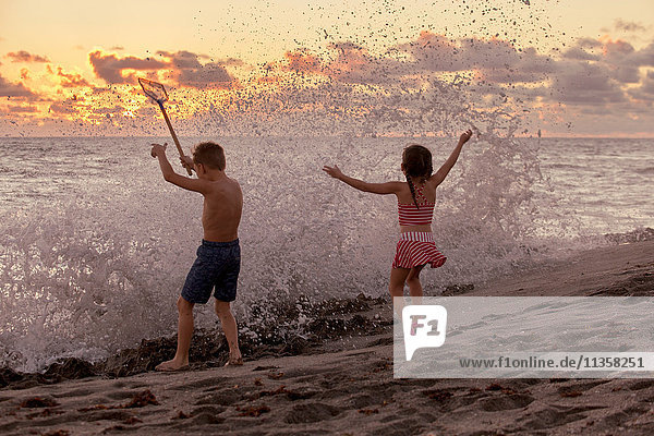 Rückansicht eines Jungen und einer Schwester  die bei Sonnenaufgang in plätschernden Wellen spielen  Blowing Rocks Preserve  Jupiter Island  Florida  USA