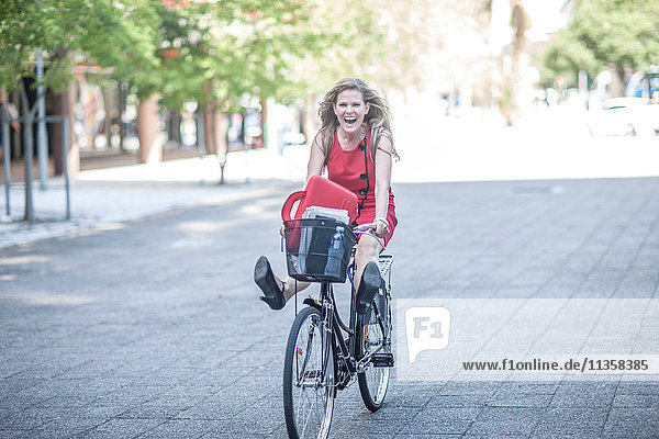 Glückliche Geschäftsfrau freilaufend auf dem Fahrrad in der Stadt