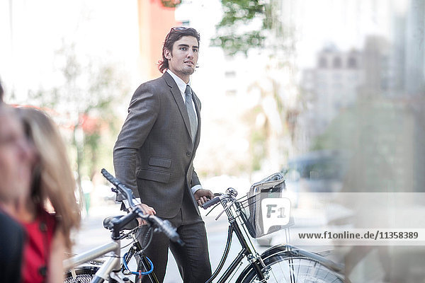 Junger selbstbewusster Geschäftsmann schiebt Fahrrad in der Stadt