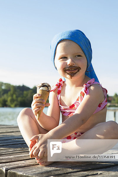 Portrait of female toddler on pier eating chocolate ice cream cone  Lake Seeoner See  Bavaria  Germany