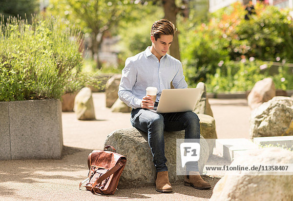 Junger Geschäftsmann liest Laptop im Stadtpark