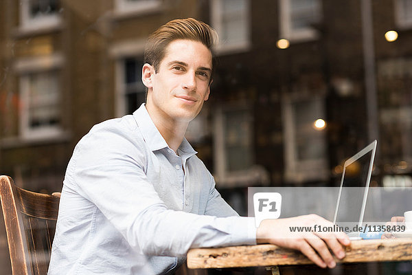 Window view of young businessman with laptop in cafe