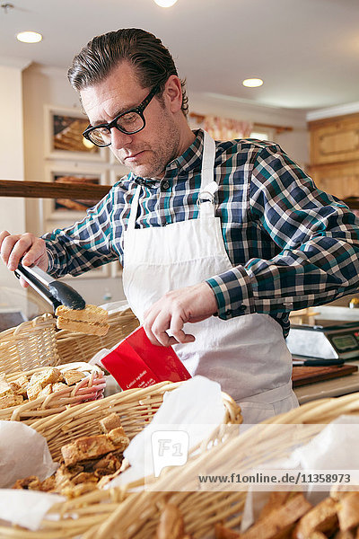 Male worker in bakery  putting fresh baked goods into paper bag for customer