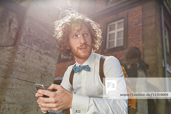Young man outdoors  using smartphone  wearing shirt and bow tie