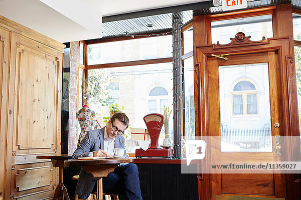 Mann sitzt im Café und schreibt in ein Notizbuch