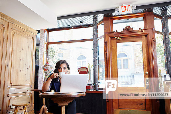 Junge Frau sitzt in Café  trinkt Kaffee  benutzt Laptop