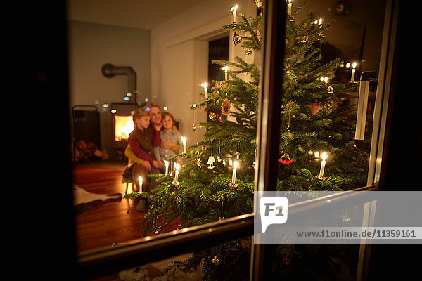 Mutter und Söhne sitzen zu Weihnachten zu Hause und schauen auf den beleuchteten Weihnachtsbaum