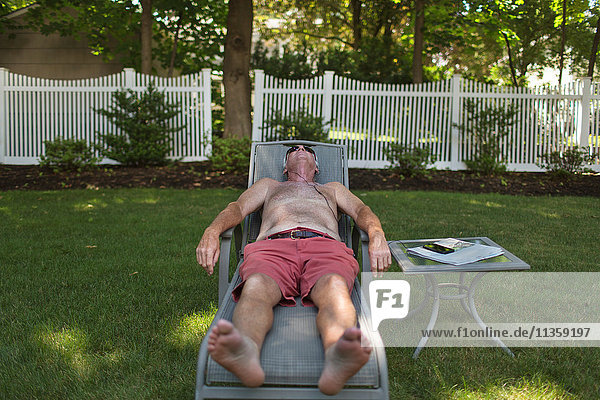 Älterer Mann beim Sonnenbaden auf einer Gartenliege und beim Hören von Kopfhörern