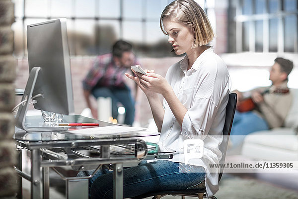 Junge Frau zu Hause  am Schreibtisch arbeitend  mit Smartphone