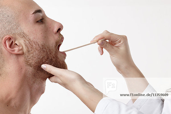 Arzt  der den Mund des Patienten mit einem Spatel untersucht