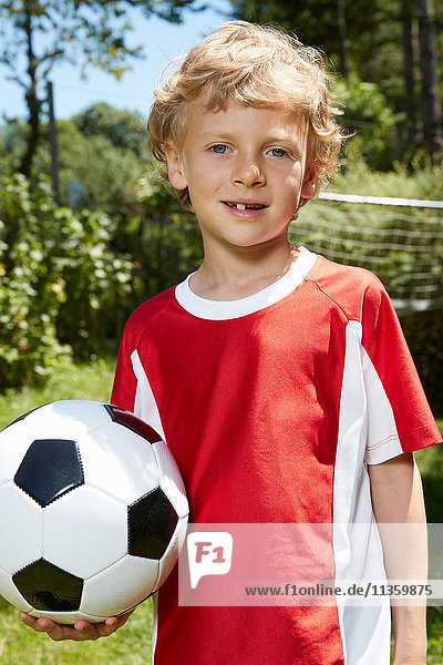Close up portrait of boy wearing soccer uniform holding soccer ball in garden