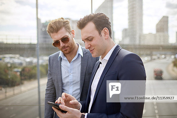 Two businessmen on footbridge texting on smartphone  London  UK
