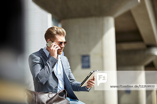 Young businessman talking on smartphone and using digital tablet in city  London  UK