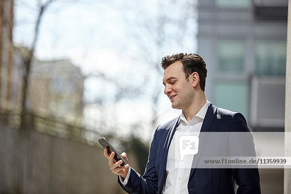 Businessman reading smartphone texts outside office  London  UK