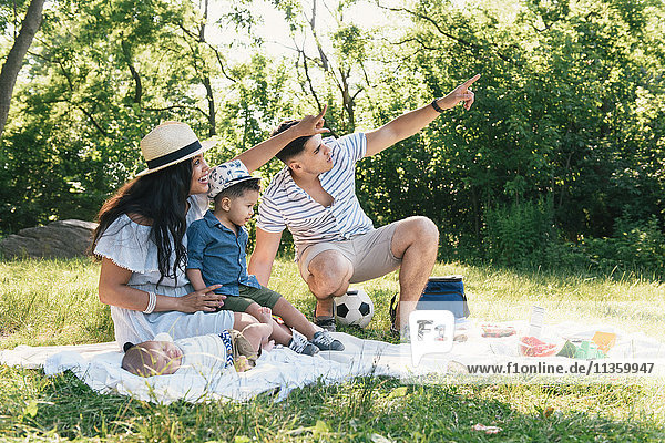 Eltern zeigen mit Säuglingen und Kleinkindern auf eine Picknickdecke im Pelham Bay Park Bronx New York USA