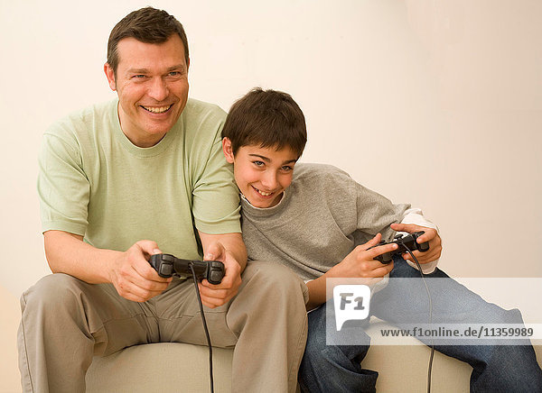 Junge und Vater spielen mit Videospiel-Controllern auf dem Sofa