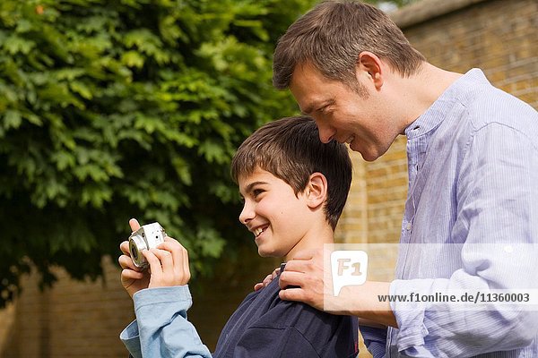 Reifer Mann erklärt seinem Sohn im Garten die Digitalkamera